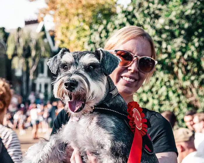 A woman holding a small show dog with a red ribbon attached. Picture used by MagnaWavePEMF