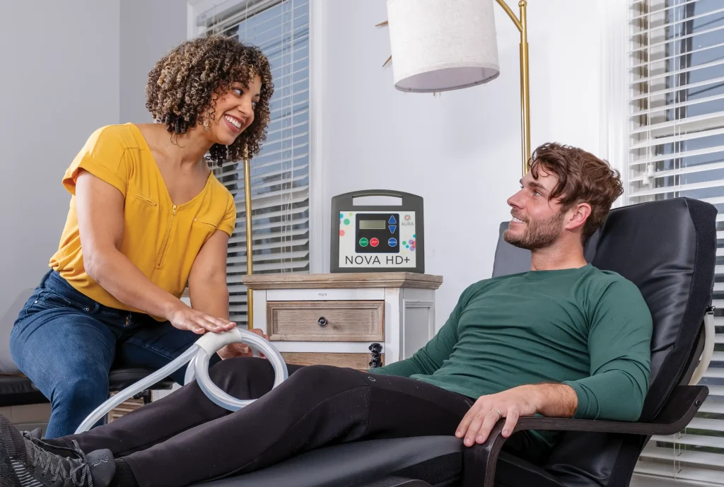 A man sitting in a reclined chair with a woman next to him applying PEMF therapy to his knee, using the Butterfly Loop PEMF attachment from MagnaWavePEMF.